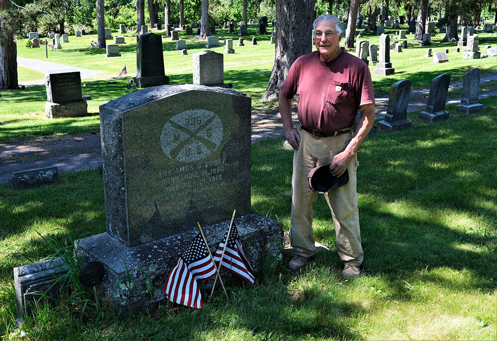 Dennis Bragg stands beside the grave of Pvt. Amos D. Scott, who died in France in 1918.
